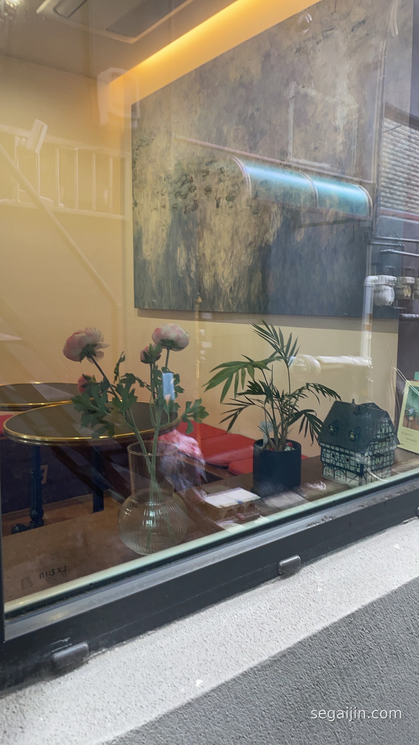 A quiet cafe window on a rainy day, with flowers, a plant and a painting