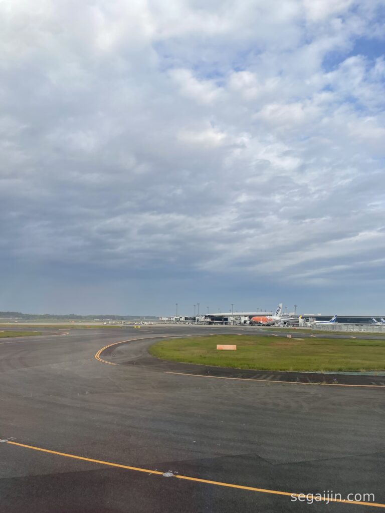 Airplanes parked at an airport terminal under a wide cloudy sky, seen across a quiet runway