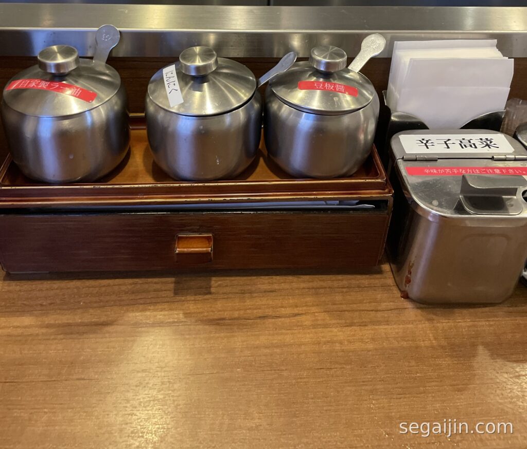 Counter condiments at a ramen shop: house chili oil, garlic, doubanjiang and spicy pickled mustard greens