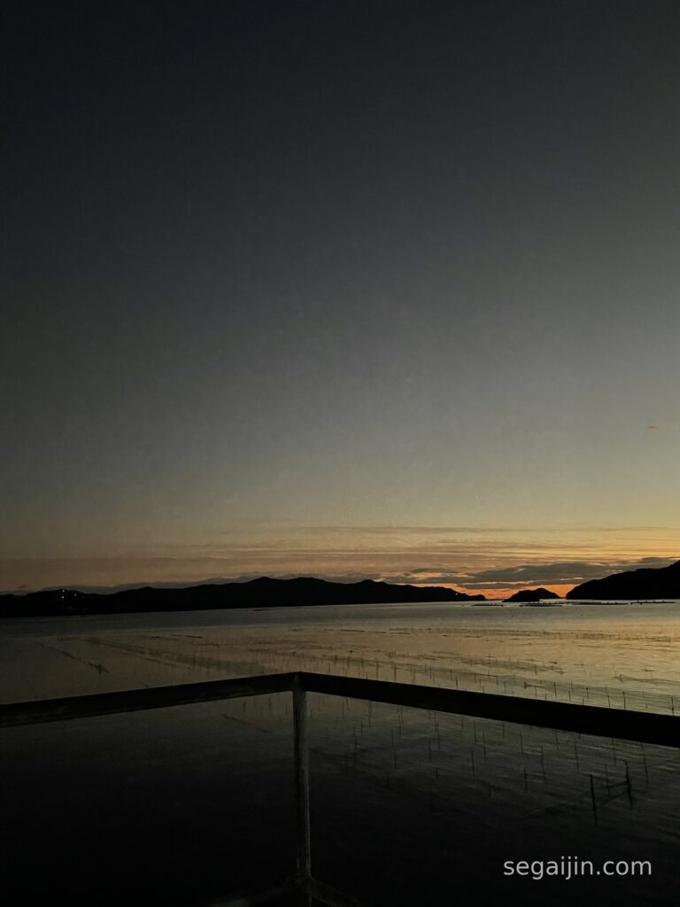 Dusk over a calm sea, with the last orange light on the horizon and a railing in the foreground