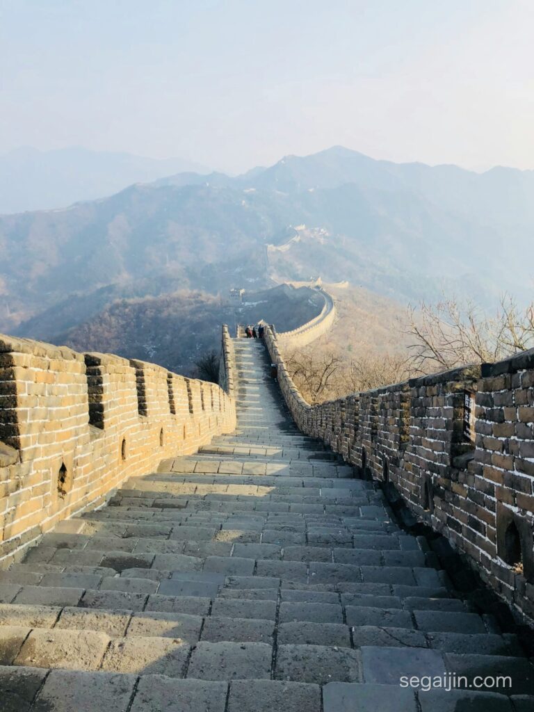 The Great Wall of China winding over misty mountain ridges, with a stone staircase in the foreground