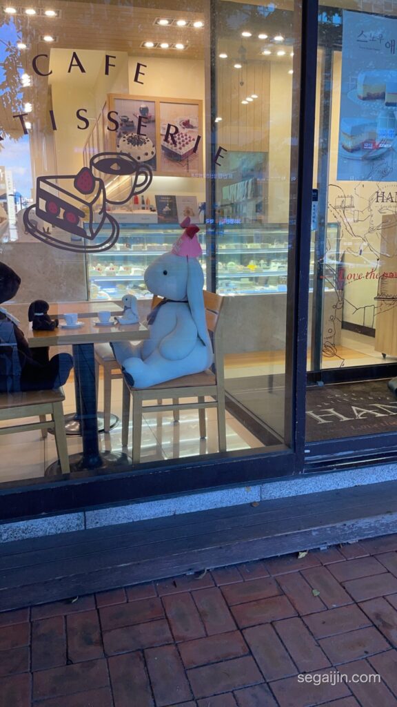 A café window with a large stuffed rabbit seated at a table for two