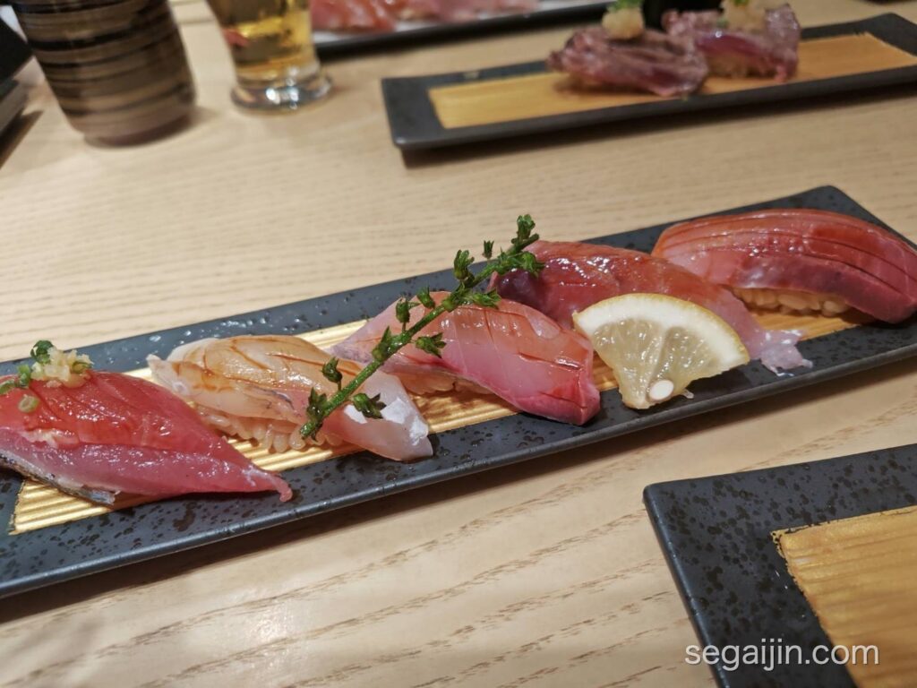 A plate of five pieces of nigiri sushi on a black and gold plate
