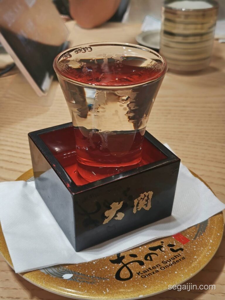 Sake in a glass sitting in a wooden masu box, on a gold Onodera plate
