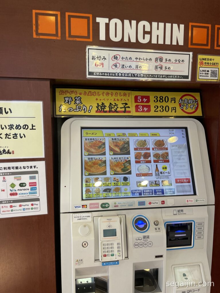 A ramen ticket machine with an English language button, a menu with ramen photos, and a sign advertising gyoza